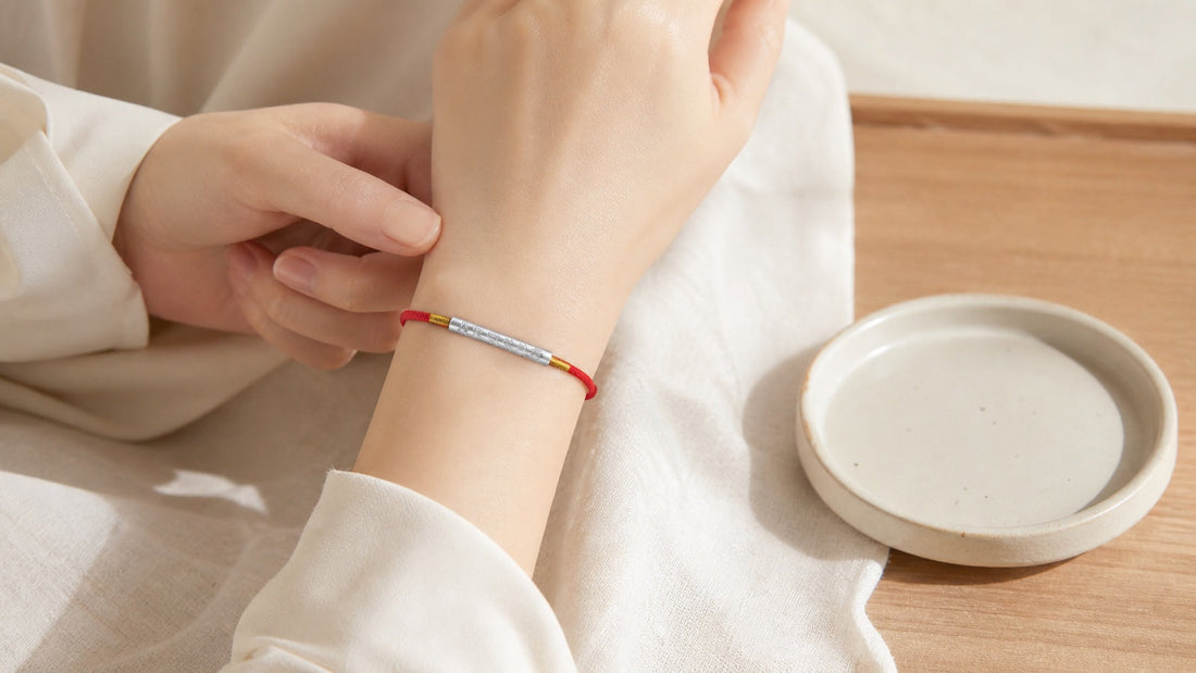 Person preparing to remove a Tibetan red string bracelet beside a ceramic jewelry tray