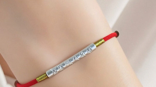 Tibetan-inspired red string bracelet with an engraved mantra tube worn on a wrist