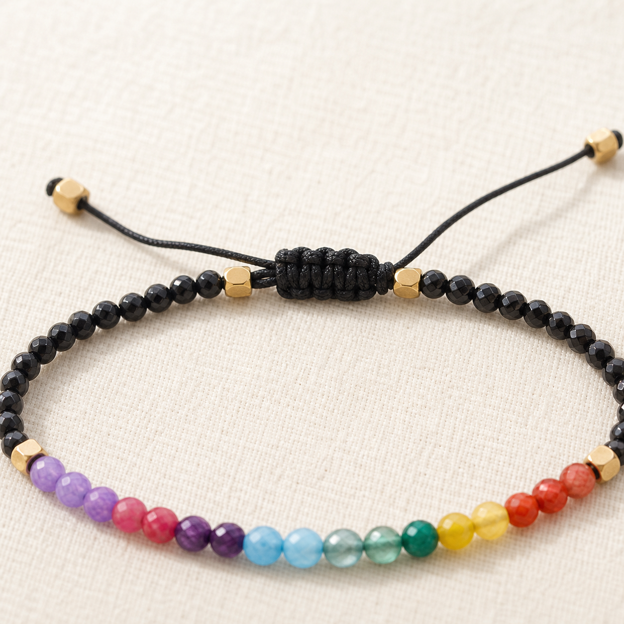 Close view of black braided sliding knot and gold-tone spacers on multicolour bead bracelet