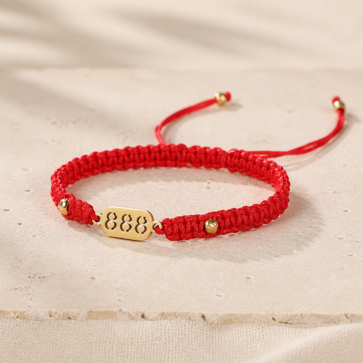 888 Angel Number Bracelet red braided cord and gold 888 plate on a warm ivory surface