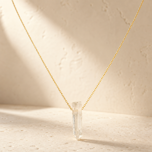 Clear quartz point necklace on warm ivory stone in natural light
