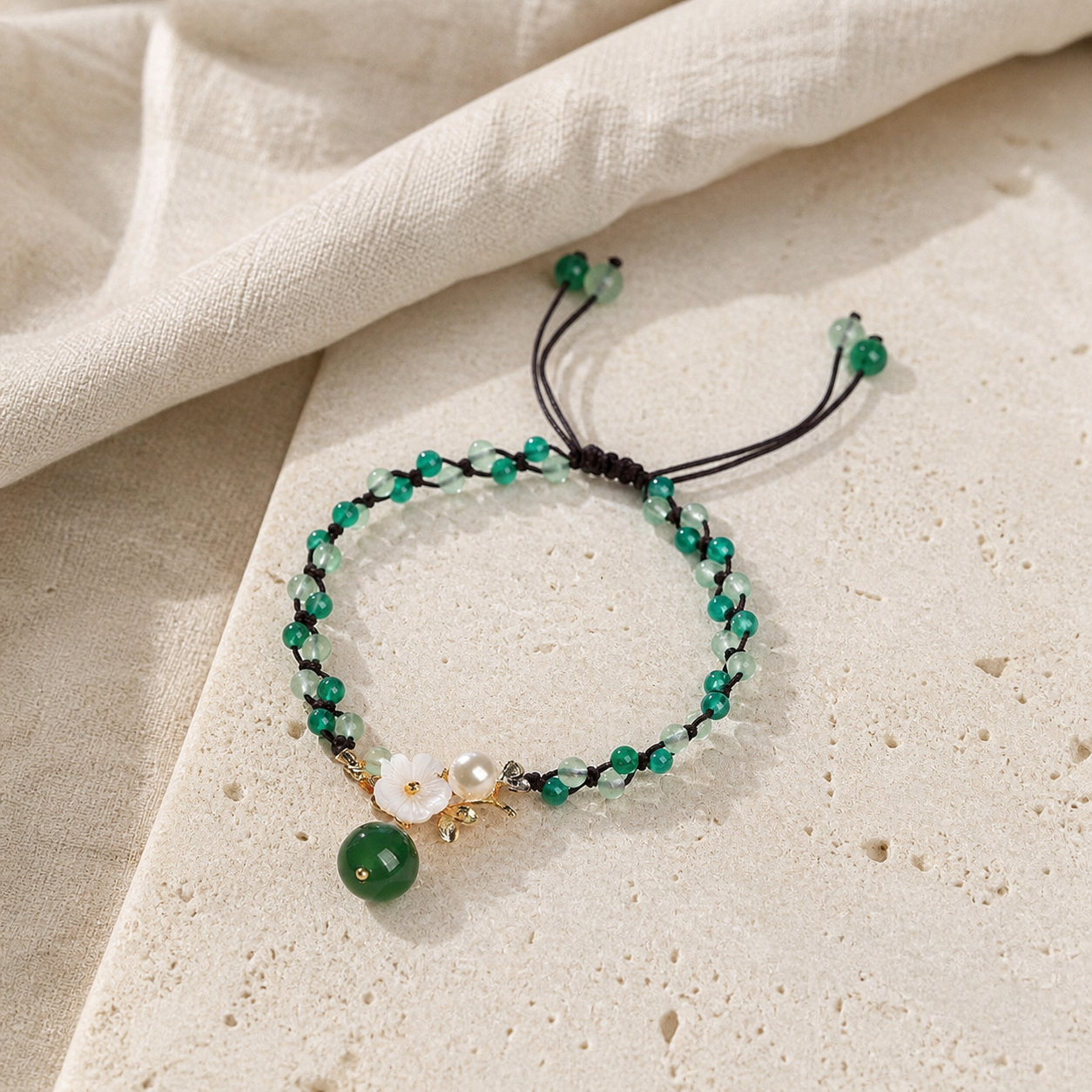 Green jade anklet with flower charm on warm ivory stone