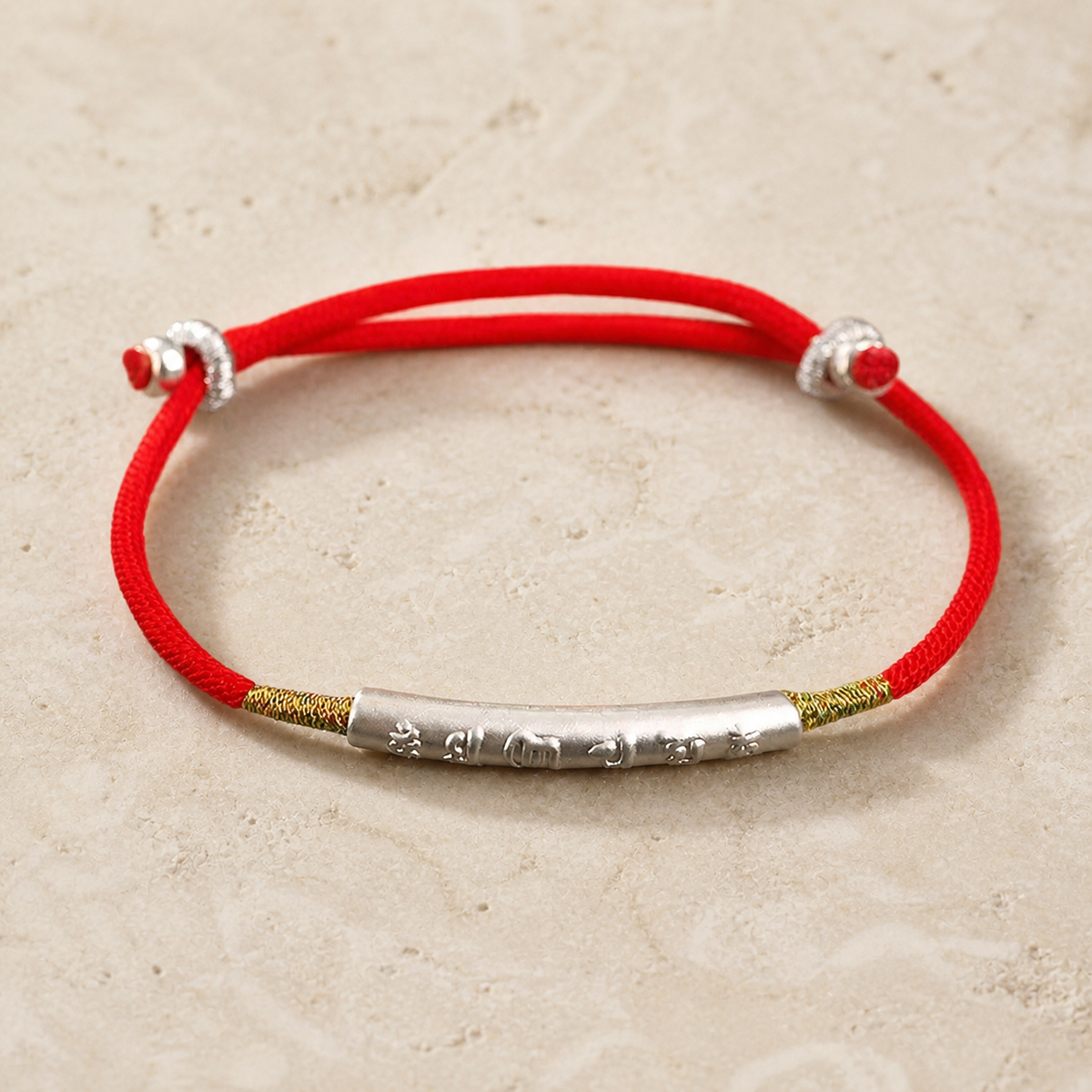 Red string bracelet laid flat showing the silver engraved tube