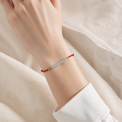 Red string bracelet with silver engraved tube worn on a wrist
